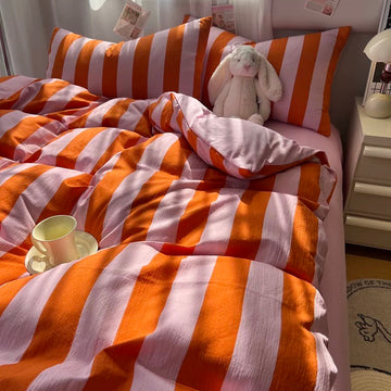 Orange and white striped bedding set on a bed, including a duvet cover and matching pillowcases, styled with a white bunny plush toy, a cup on a saucer, and a bedside lamp.