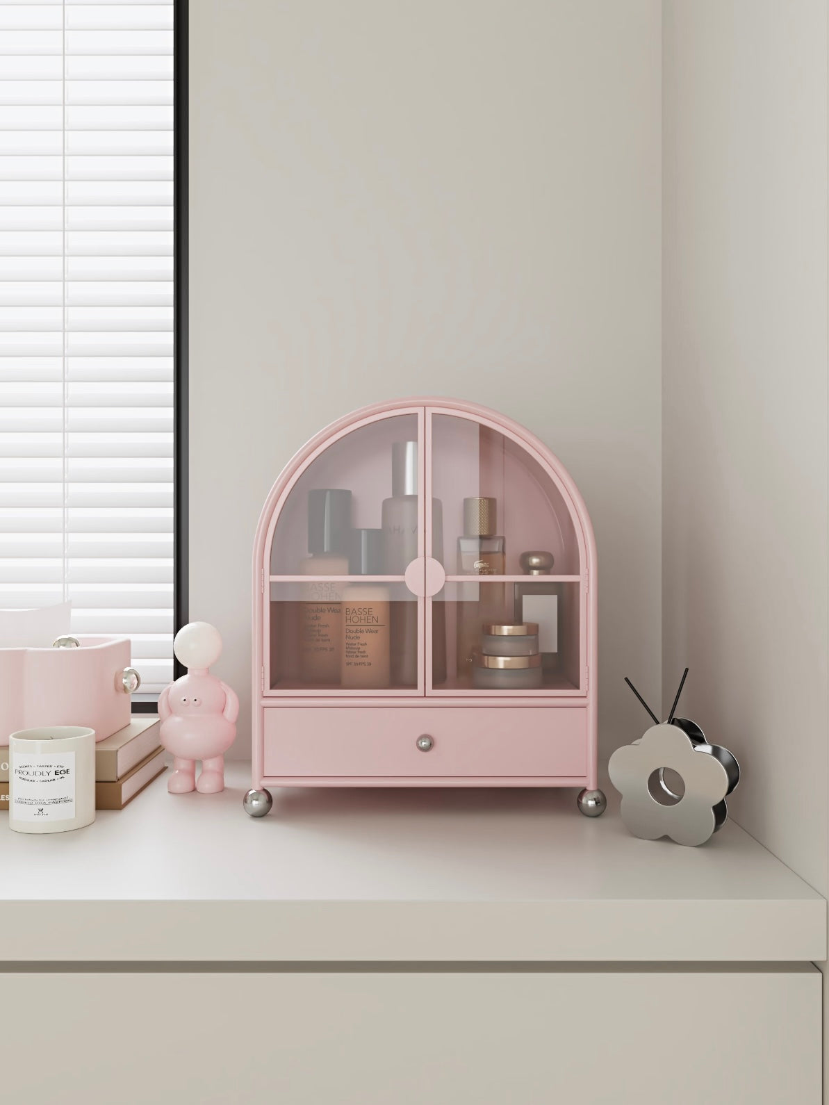 A pink perfume cabinet faces forward on a dresser, with skincare bottles visible behind the glass doors.