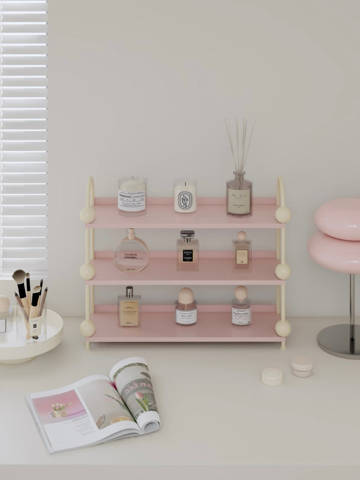 Pink perfume shelf with cream arches displays bottles and small jars across three open levels on a vanity.