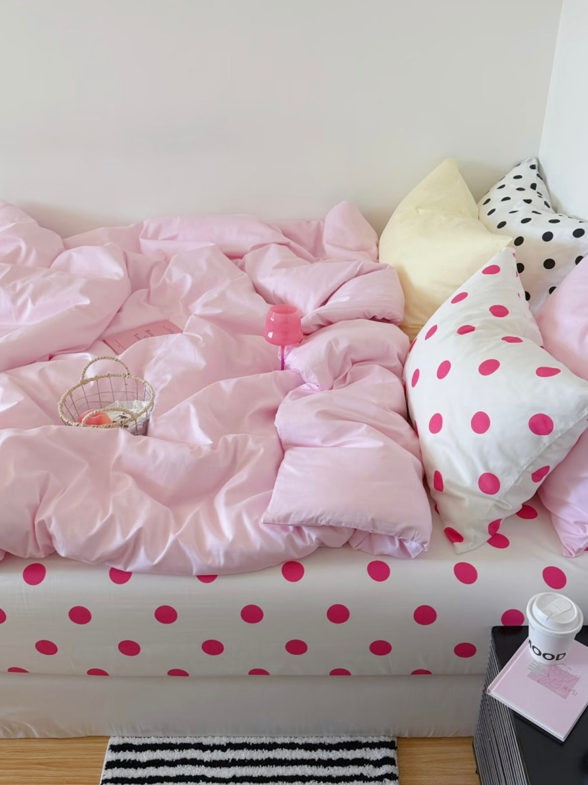 Side view of pink preppy bedding with the dotted sheet showing beneath the cover and a yellow pillow beside pink dots.