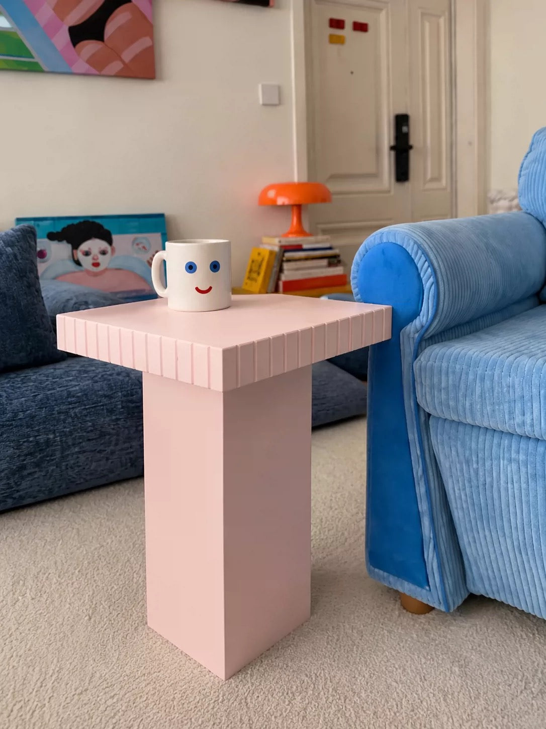 Pink sofa side table with a striped edge top beside a blue sofa on a cream rug