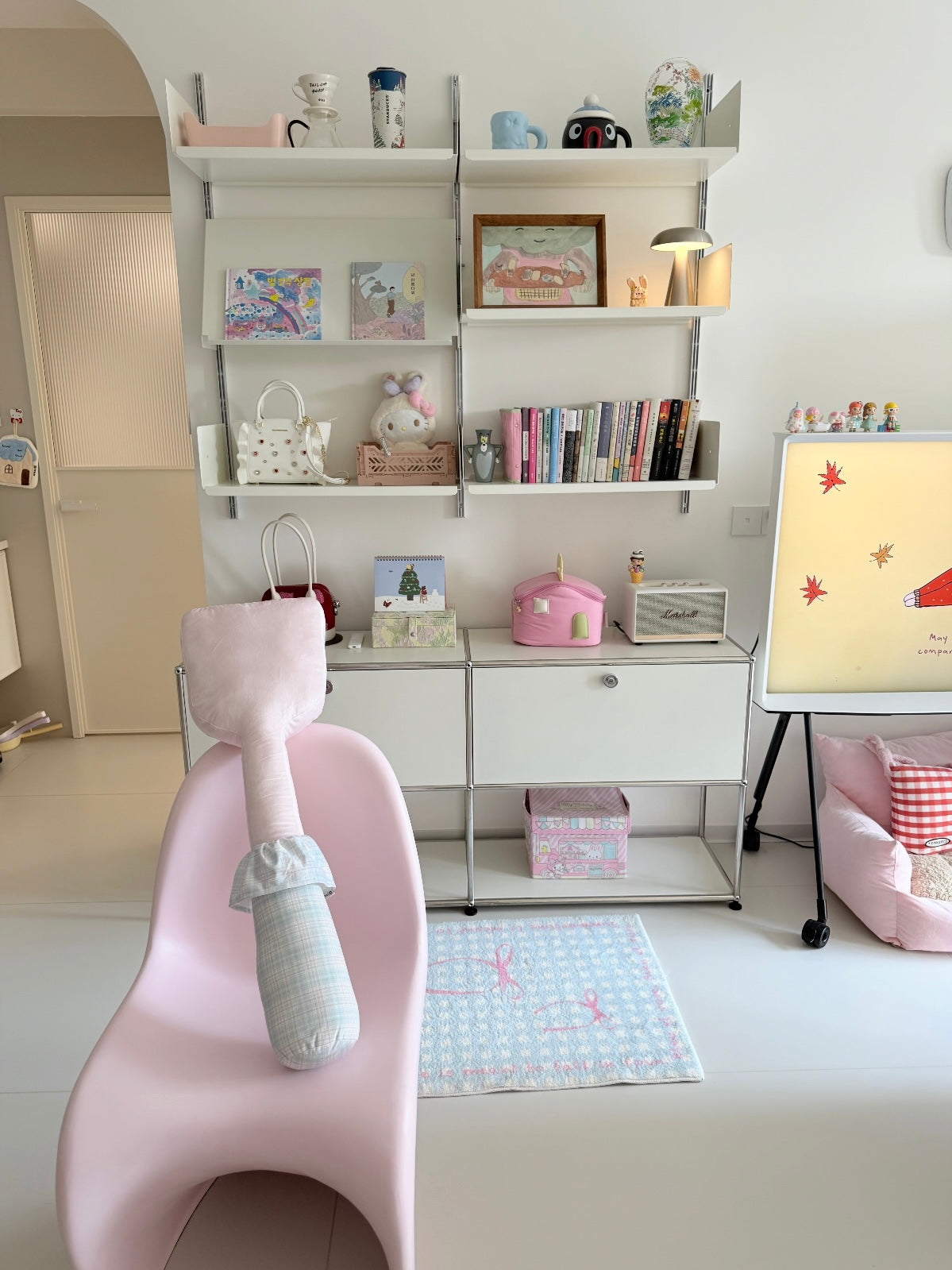 A pink spatula pillow rests upright against a pink chair, with its pale handle hanging down toward the seat.