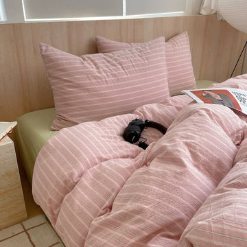 Bed with pink striped bedding and pillows in a room with wooden walls.