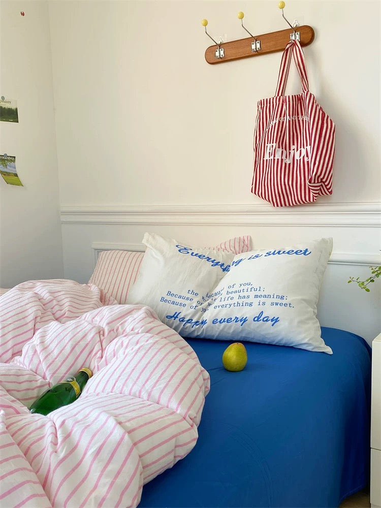 Bedroom with pink striped bedding, blue blanket, and pillows with text.
