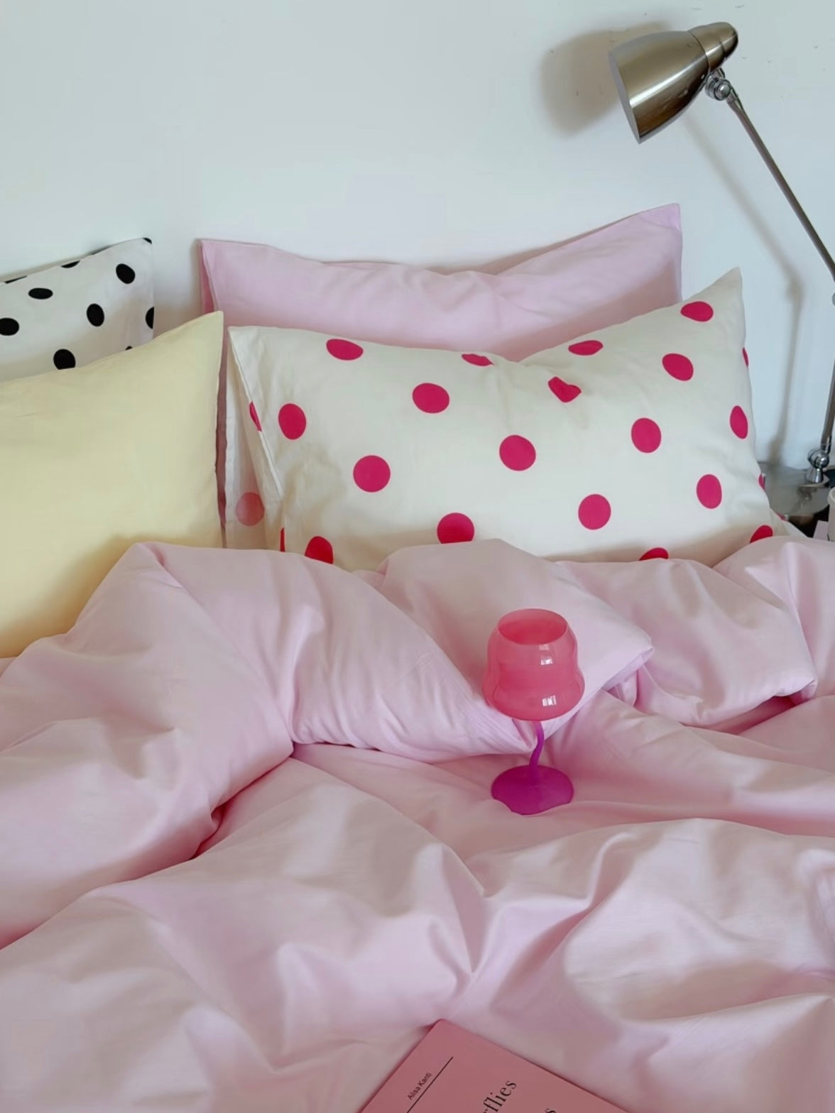 Pink and yellow bedding with a fuchsia dot pillowcase and a pink glass on the plain duvet cover.