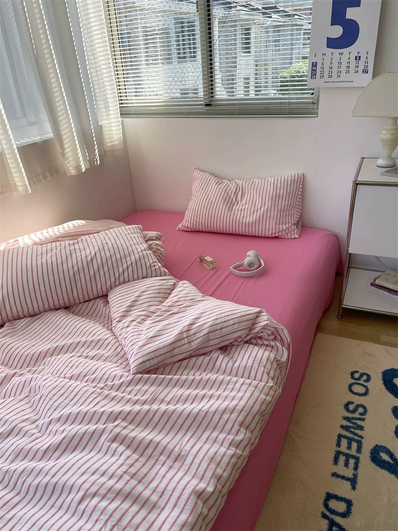 Pink bed with striped bedding in a room with a window and calendar.