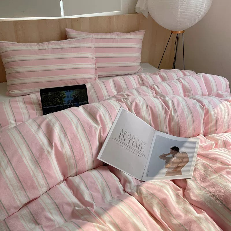 Pink striped bedding with a tablet and book on a bed