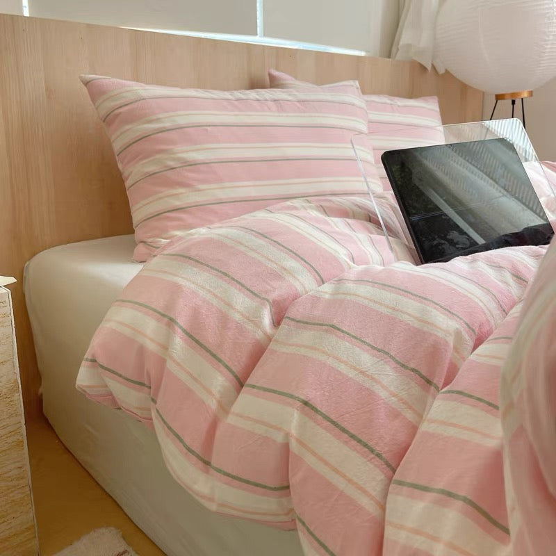 Pink striped bedding on a bed with a tablet on top
