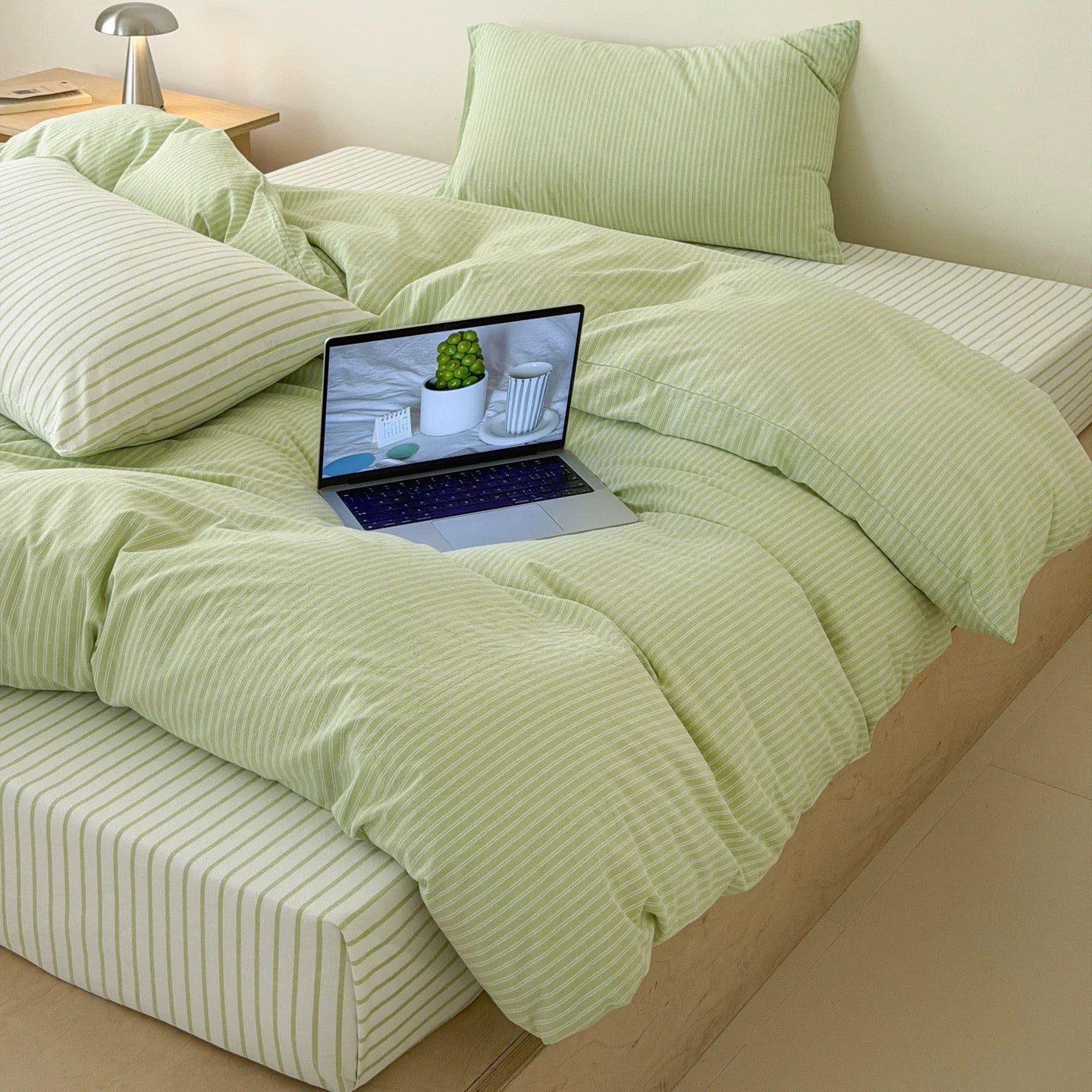 Korean minimal bedroom styled using pastel green striped bedding with clean neutral furniture and warm lighting accents.