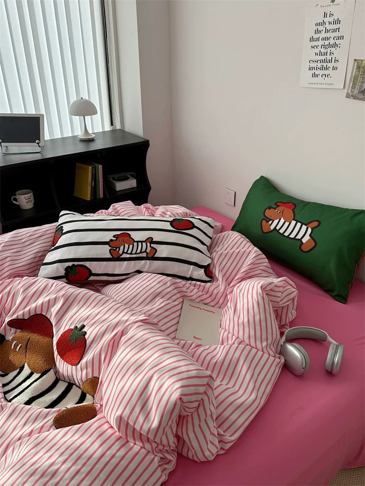 Bed with pink and white striped bedding featuring cartoon characters, next to a small table with decorative items.