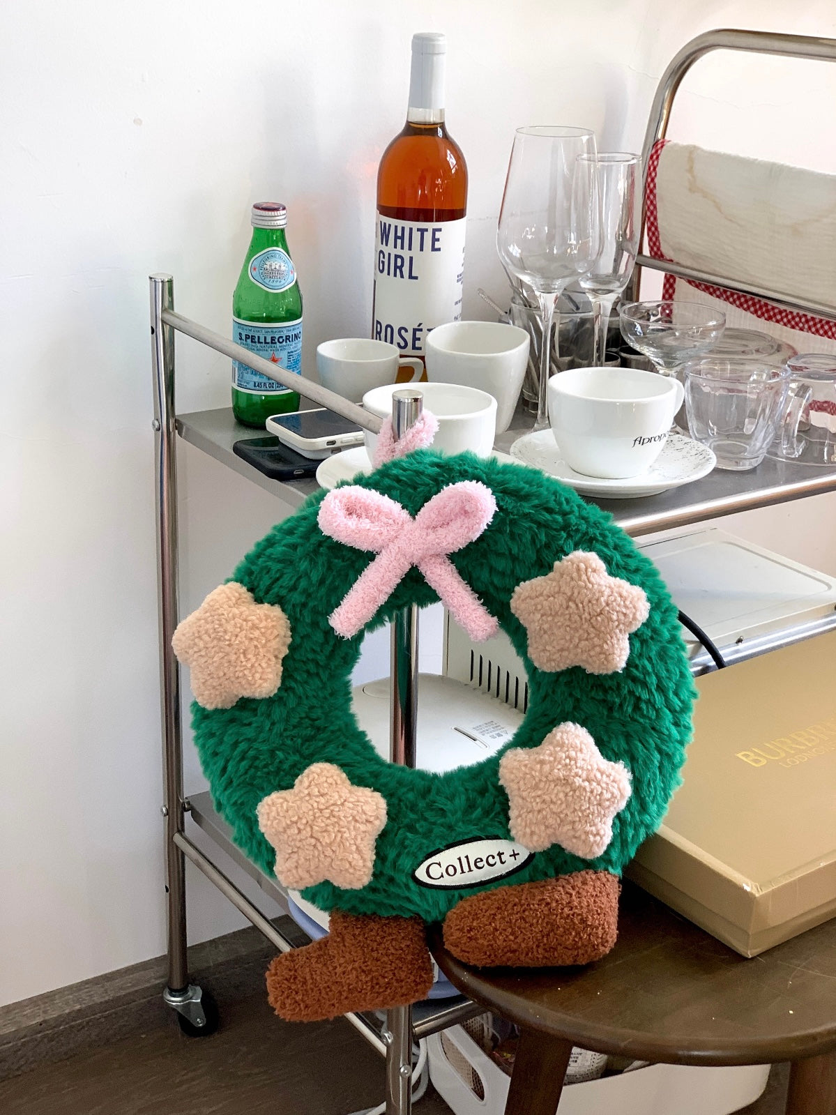 Plush Christmas wreath pillow with pink bow and star accents styled beside a metal storage cart