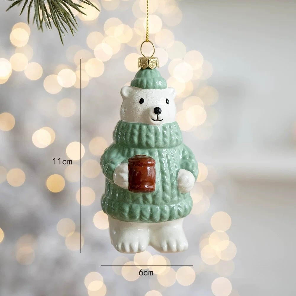 A polar bear ornament wears a green hat and a sweater with raised details while holding a brown mug.