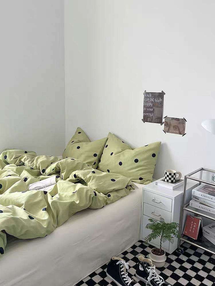 Bedroom with green polka dot bedding and a nightstand with books and a plant.