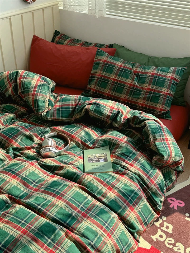 Plaid blanket and pillows on a bed with a cup and book.