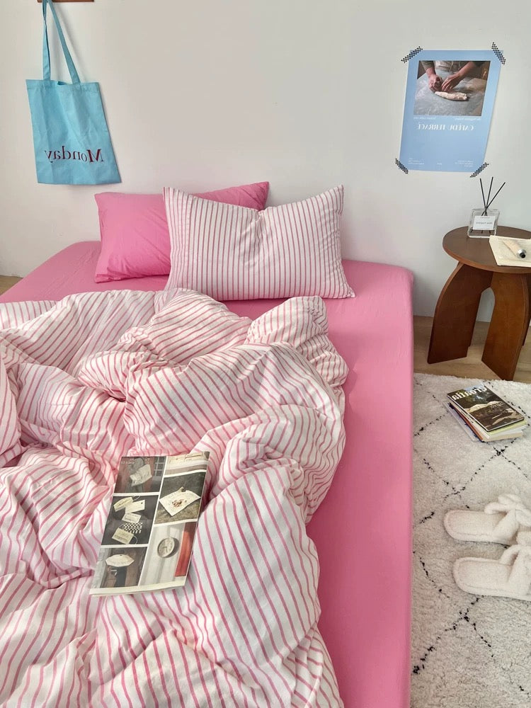 Bed with pink and white striped bedding, pillows, and books on a light gray wall background.