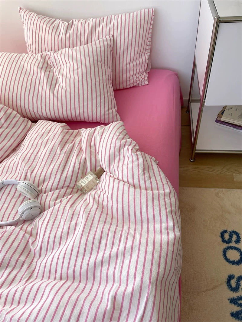 Pink bed with striped bedding and pillows in a room setting.