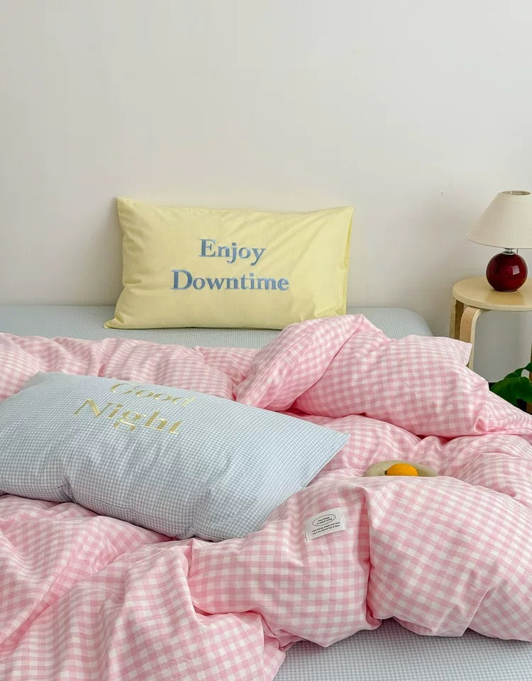 Bed with pink checkered bedding and pillows with text on a light gray wall background