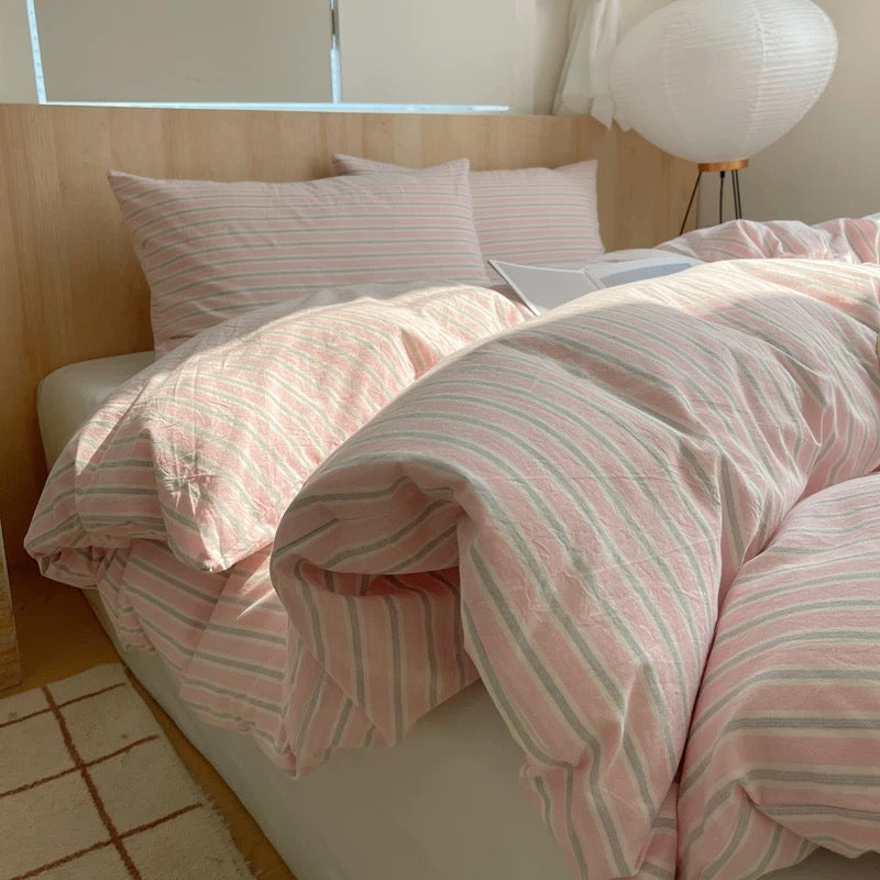 Pink and white striped bedding on a bed with a wooden headboard.
