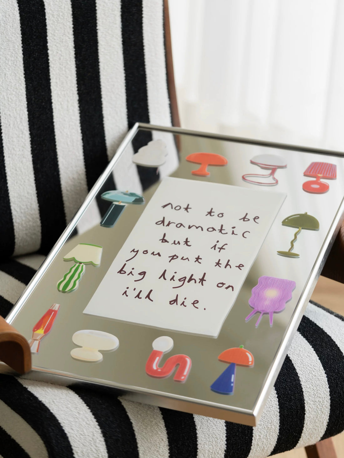 Mirror wall art with colorful lamp illustrations and handwritten text in a slim silver frame beside a sofa.