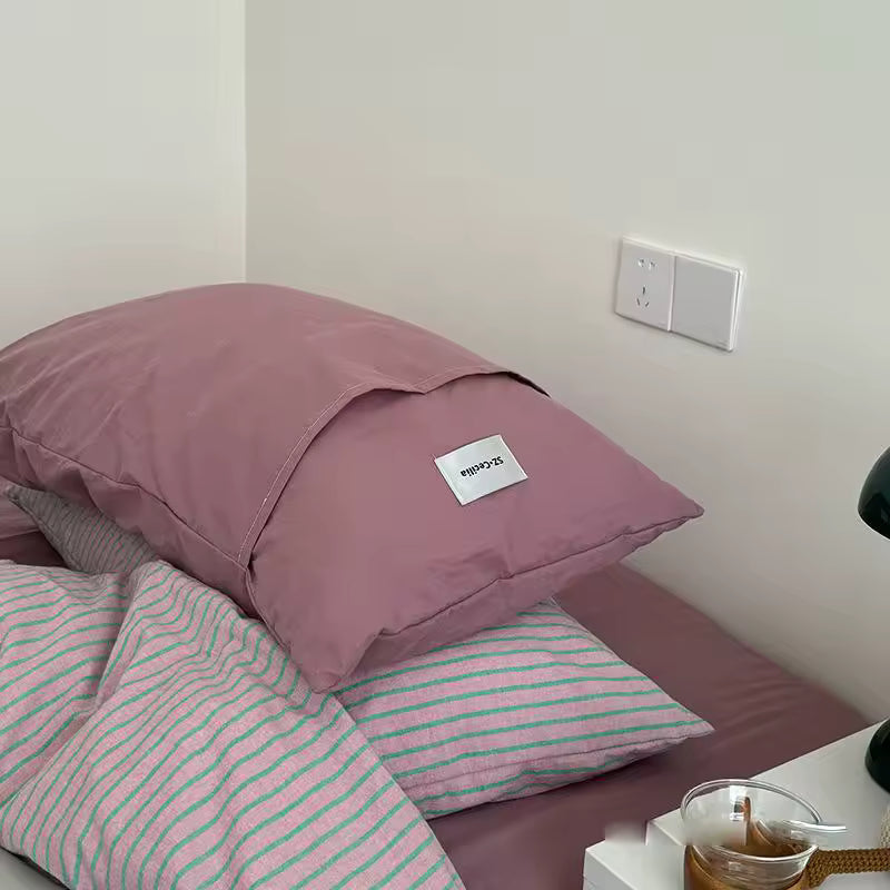 Pink pillow with a brand label on a bed with striped bedding.