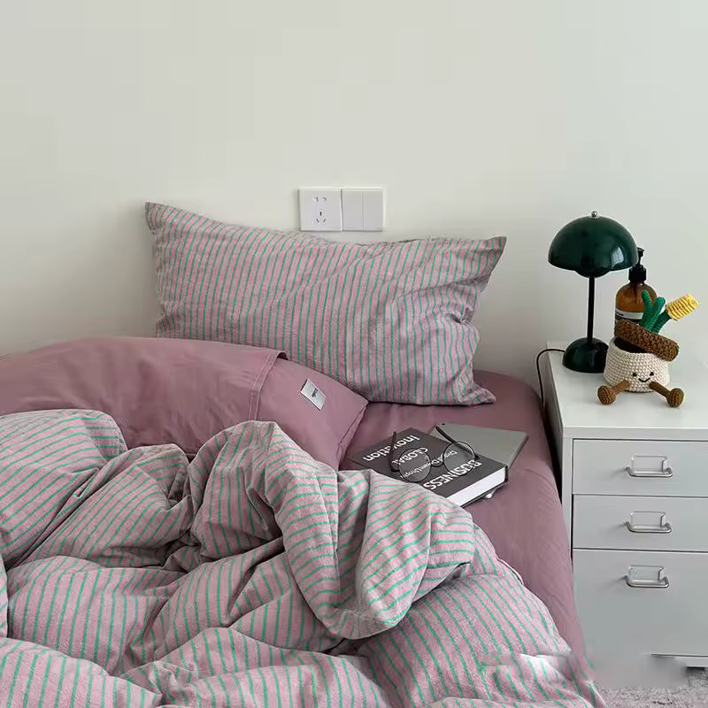 Bed with pink and white striped bedding and pillows, nightstand with lamp and plush toy.