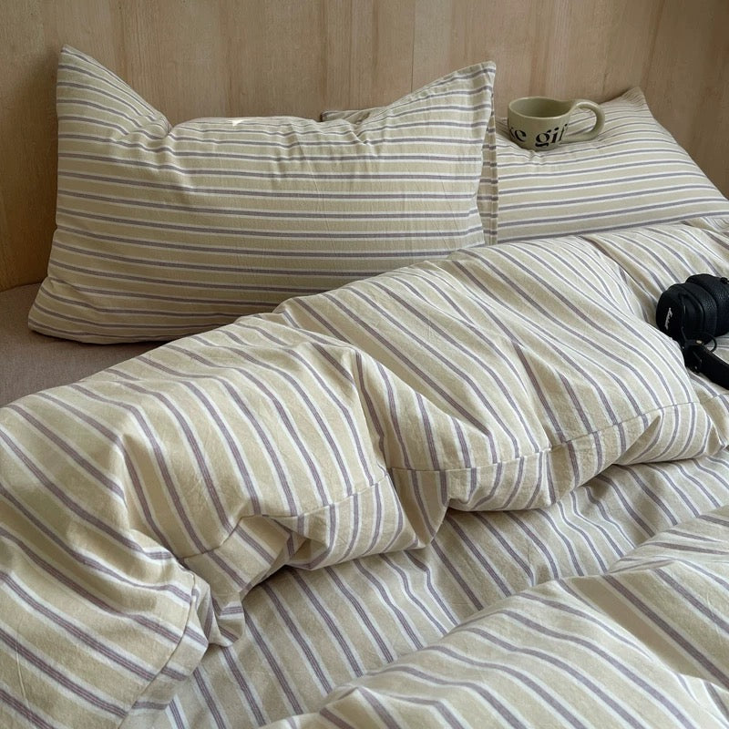 Striped bedding with pillows and a mug on a wooden bed frame.