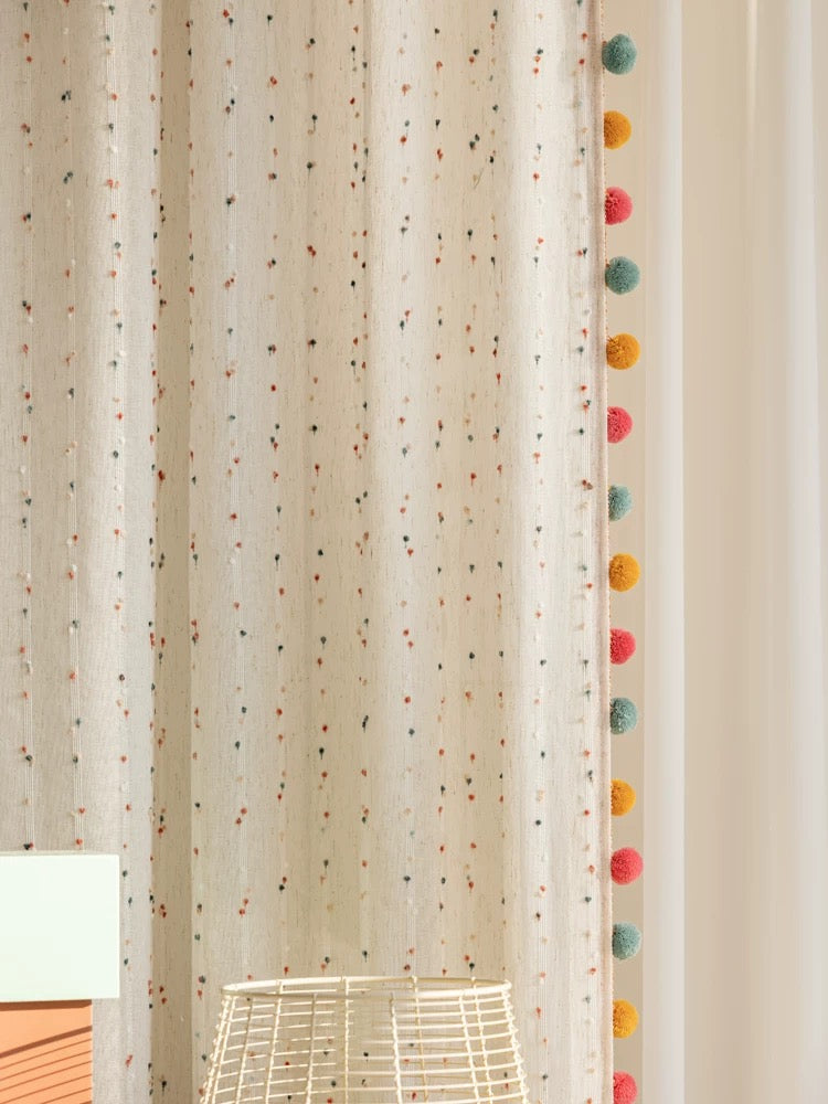 Boho living room window styled with rainbow embroidered pom-pom curtains.
