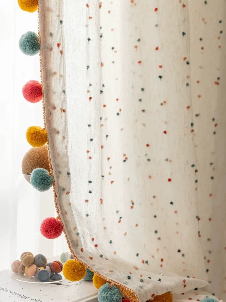 Sheer curtain with colorful pom-poms on a white background
