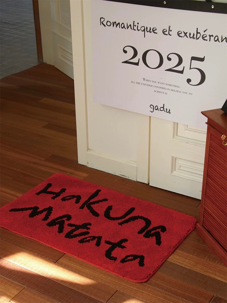 A red bath mat with black Hakuna Matata lettering lies in front of a large calendar near the doorway.