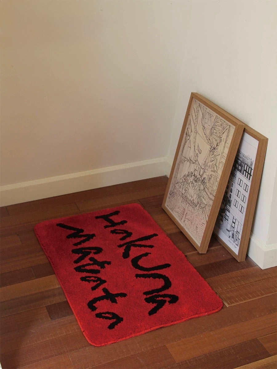 A red lettering rug shows black Hakuna Matata script across its rectangular surface from a front angle.