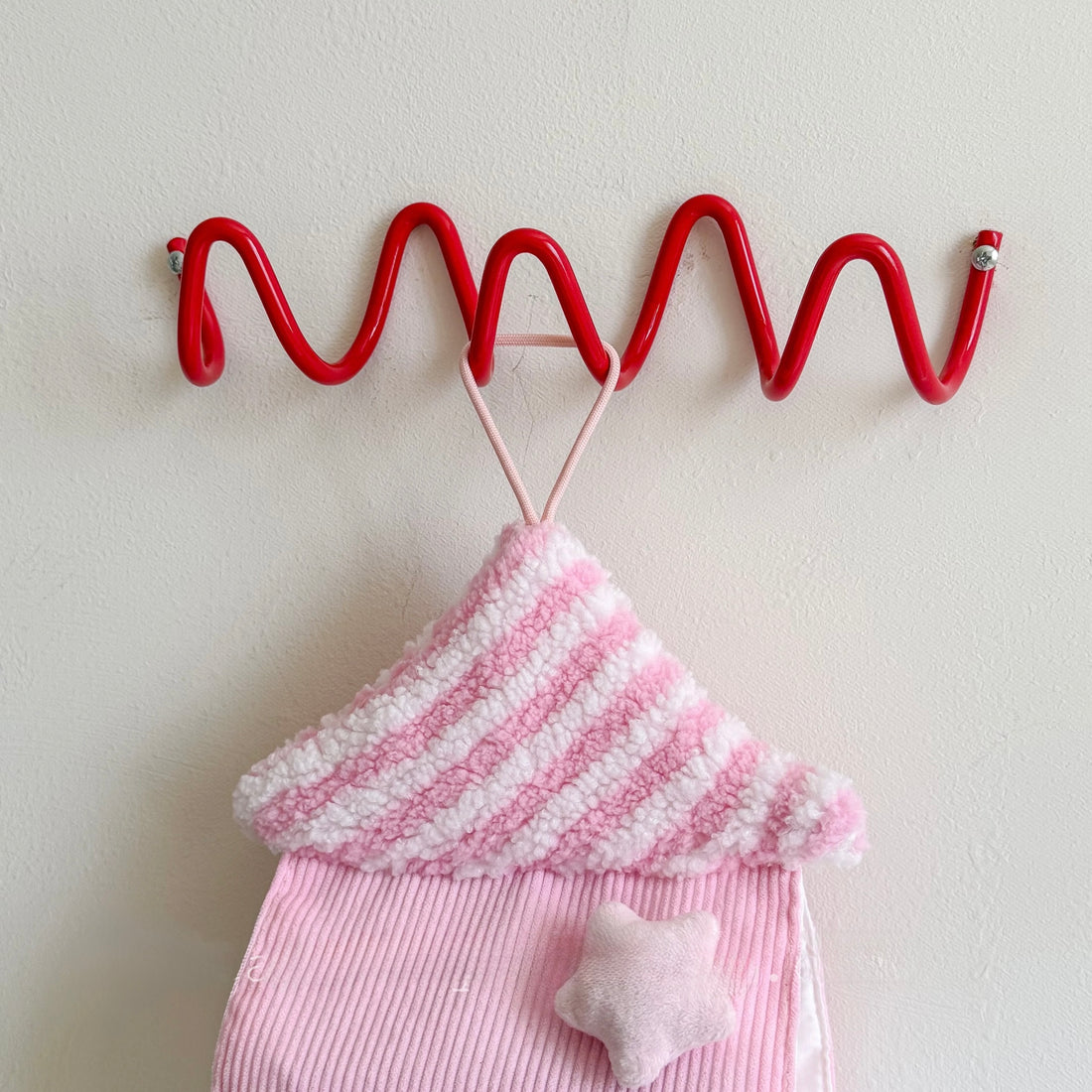 Red wavy hook with pink and white striped fabric and star-shaped object on a light background