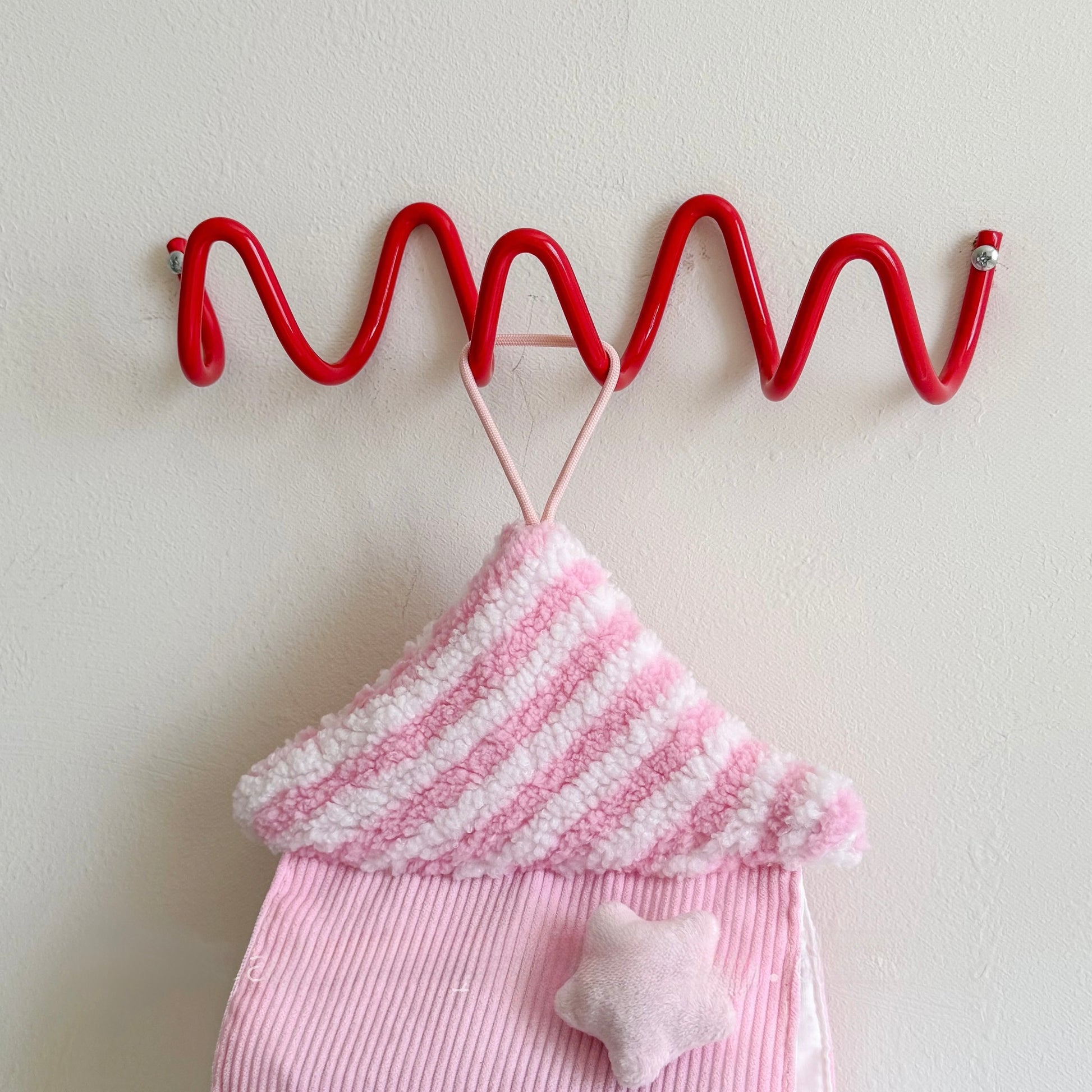 Red wavy hook with pink and white striped fabric and star-shaped object on a light background