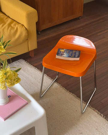 Orange chair with a book on a wooden floor next to a yellow couch.