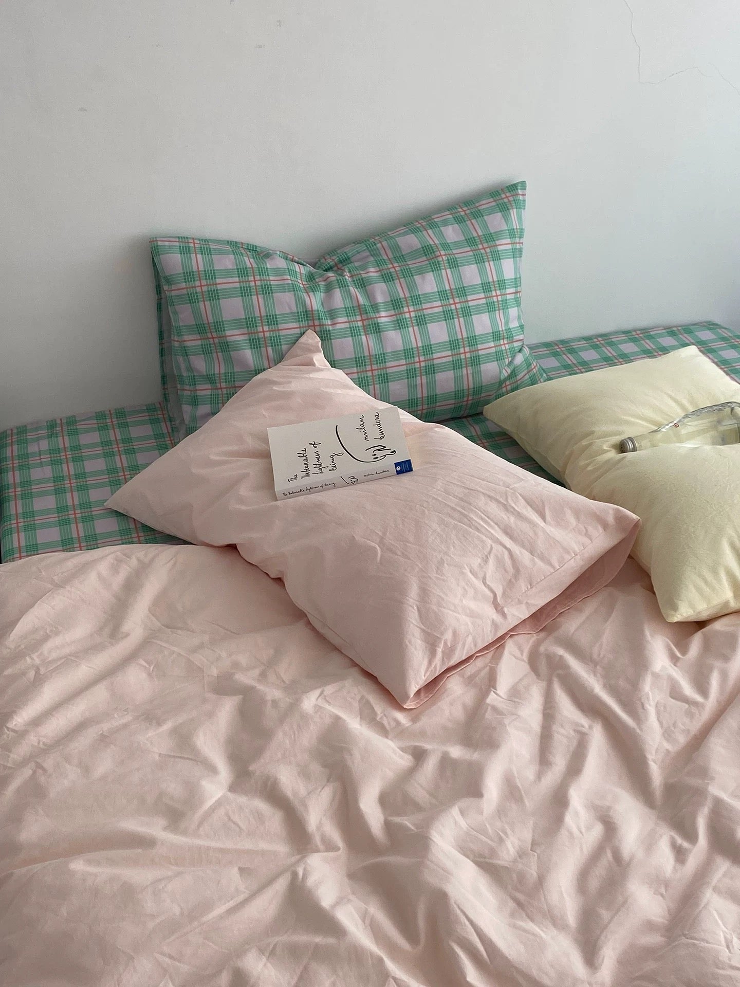 Bed with pink bedding and plaid pillows against a white wall