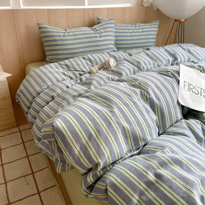Striped bedding set on a bed with pillows and a blanket in a room.