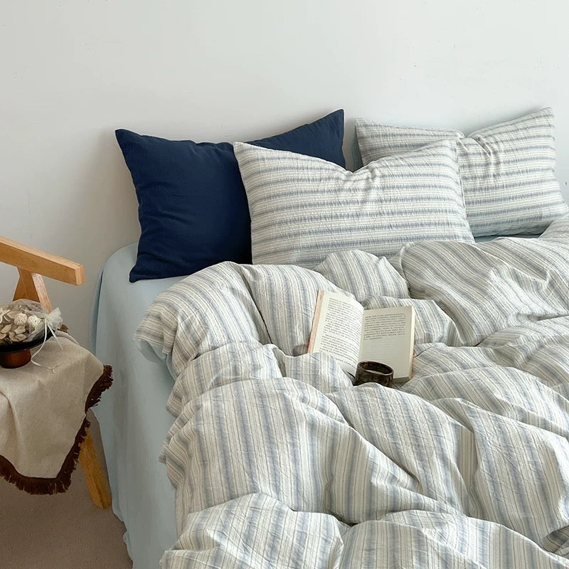 Scandinavian bedroom scene styled with a striped duvet cover, wood side table, and dried flowers