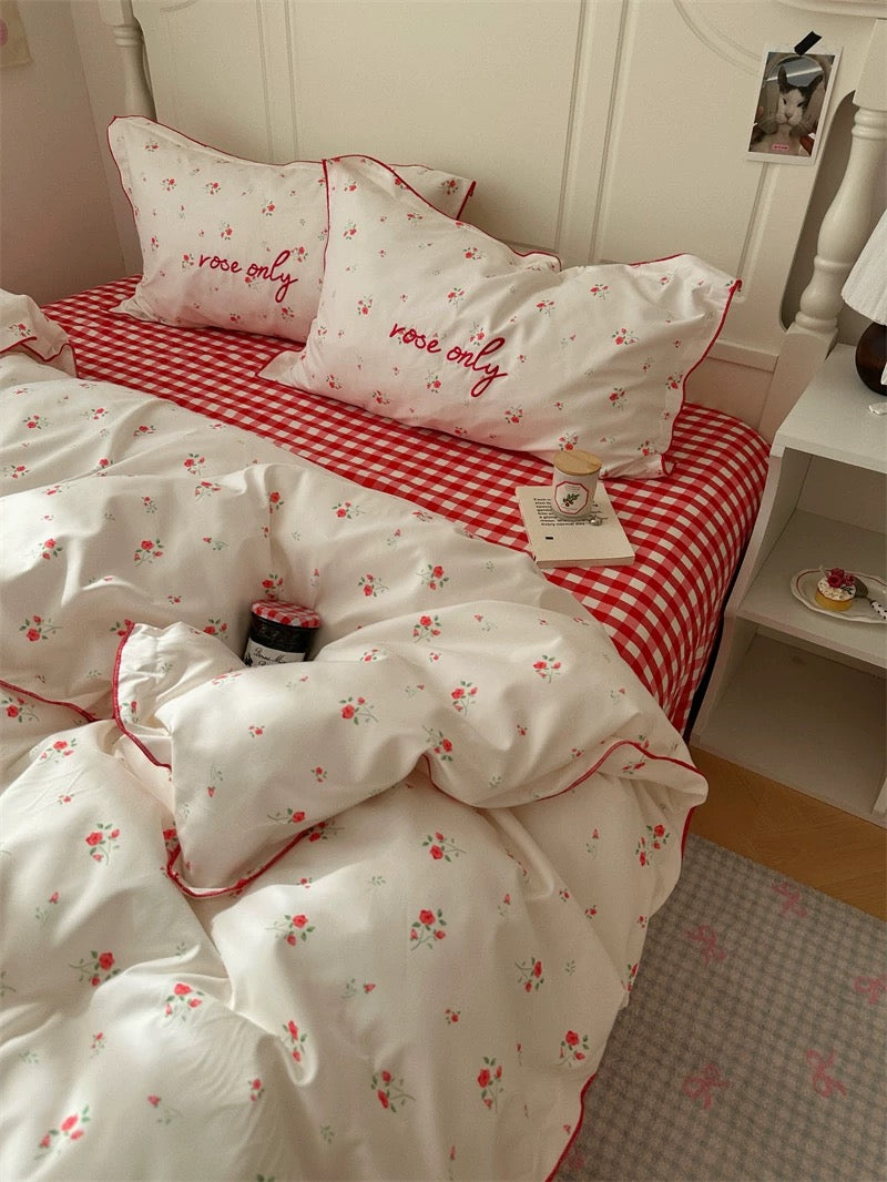 Bedding set with floral patterns and red accents on a bed with checkered sheets.
