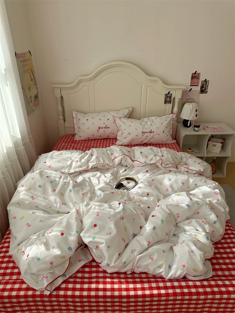 Bed with white floral comforter and red checkered bedspread in a room.