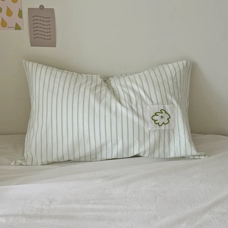 Green striped pillowcase with a stitched flower applique on a white bed.