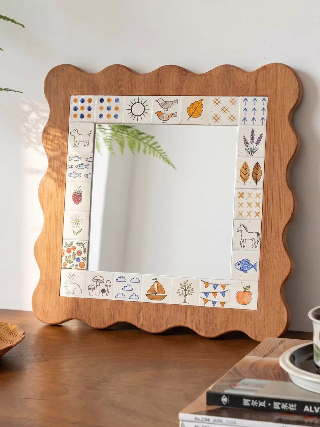 A scalloped wall mirror has a brown frame and little illustrated panels, with a fern reflected near the top.