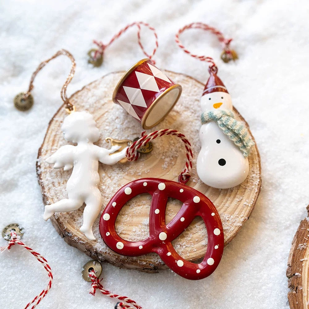 Scandinavian Christmas ornaments show a white angel, red drum, snowman and dotted red pretzel.