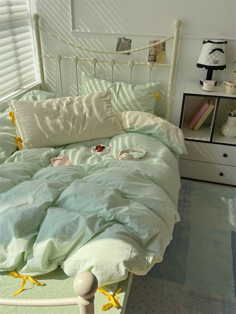 Bed with light green bedding and white pillows in a room with a window and shelf.