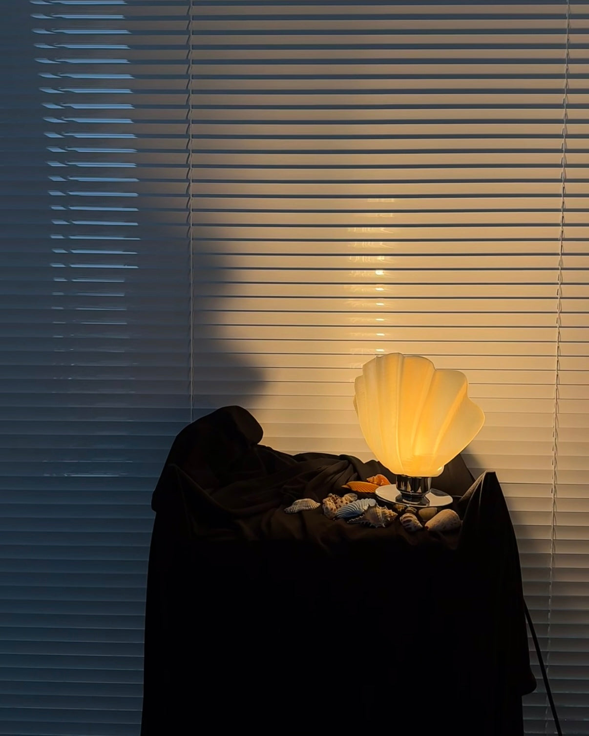Shell-shaped lamp on a surface with blinds in the background