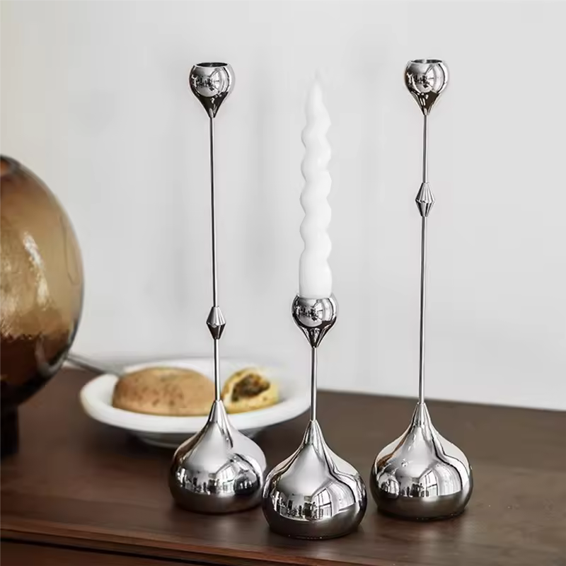 Set of three silver candle holders with a white candle on a wooden surface.
