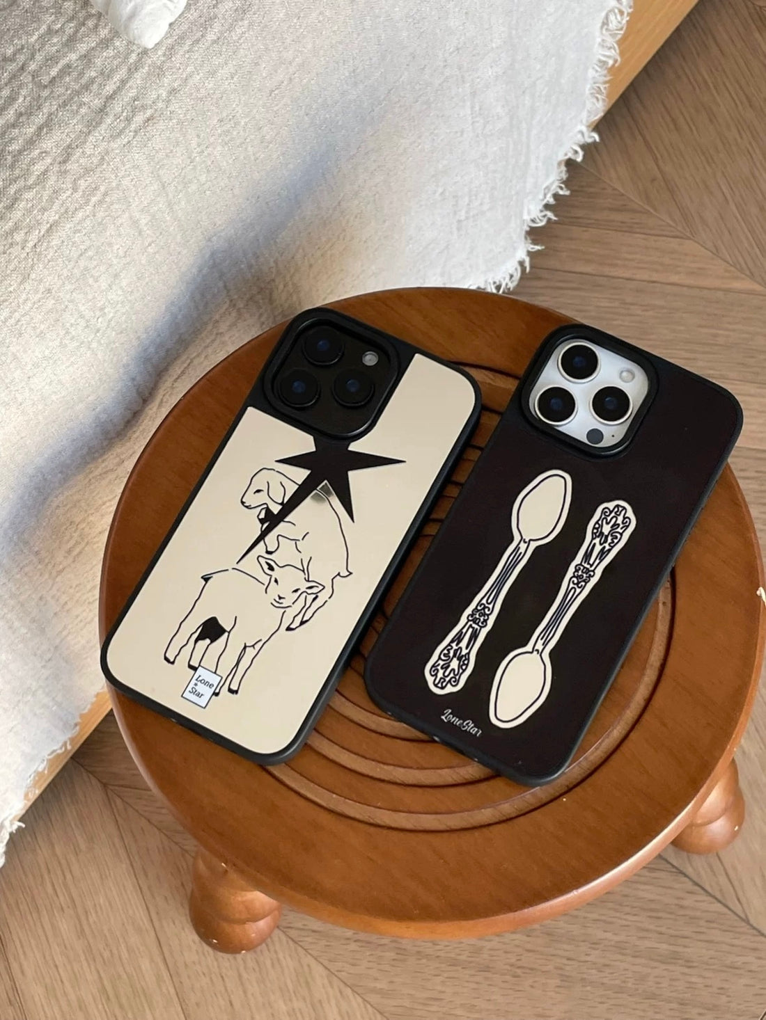 A mirror phone case in black with two vintage spoons stands beside the silver lamb and pointed star design.