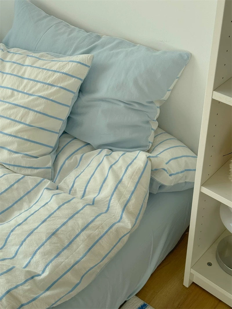 Bed with blue and white striped bedding and pillows next to a white shelf.
