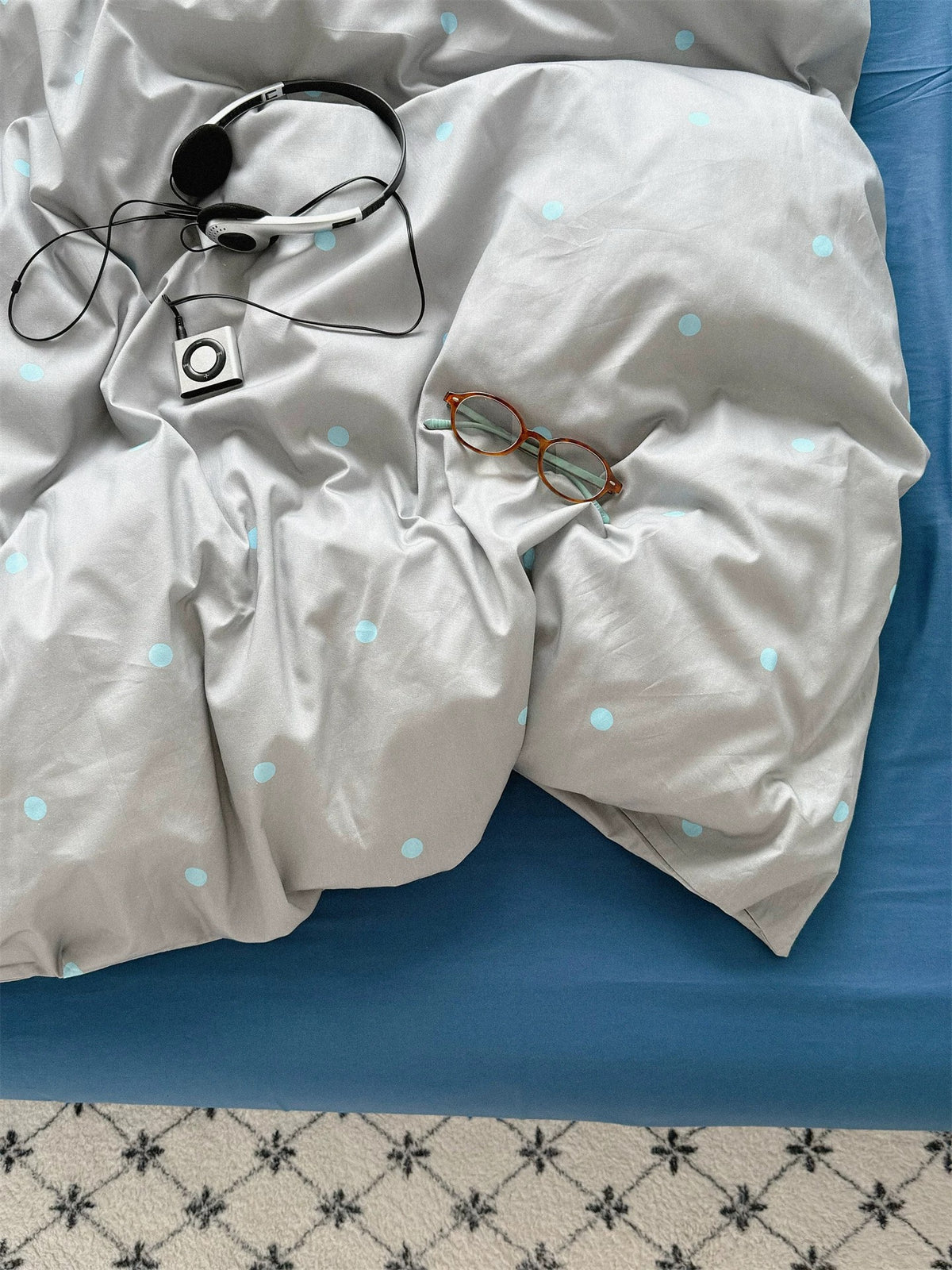 Close view of small blue dots across the rumpled gray duvet cover.