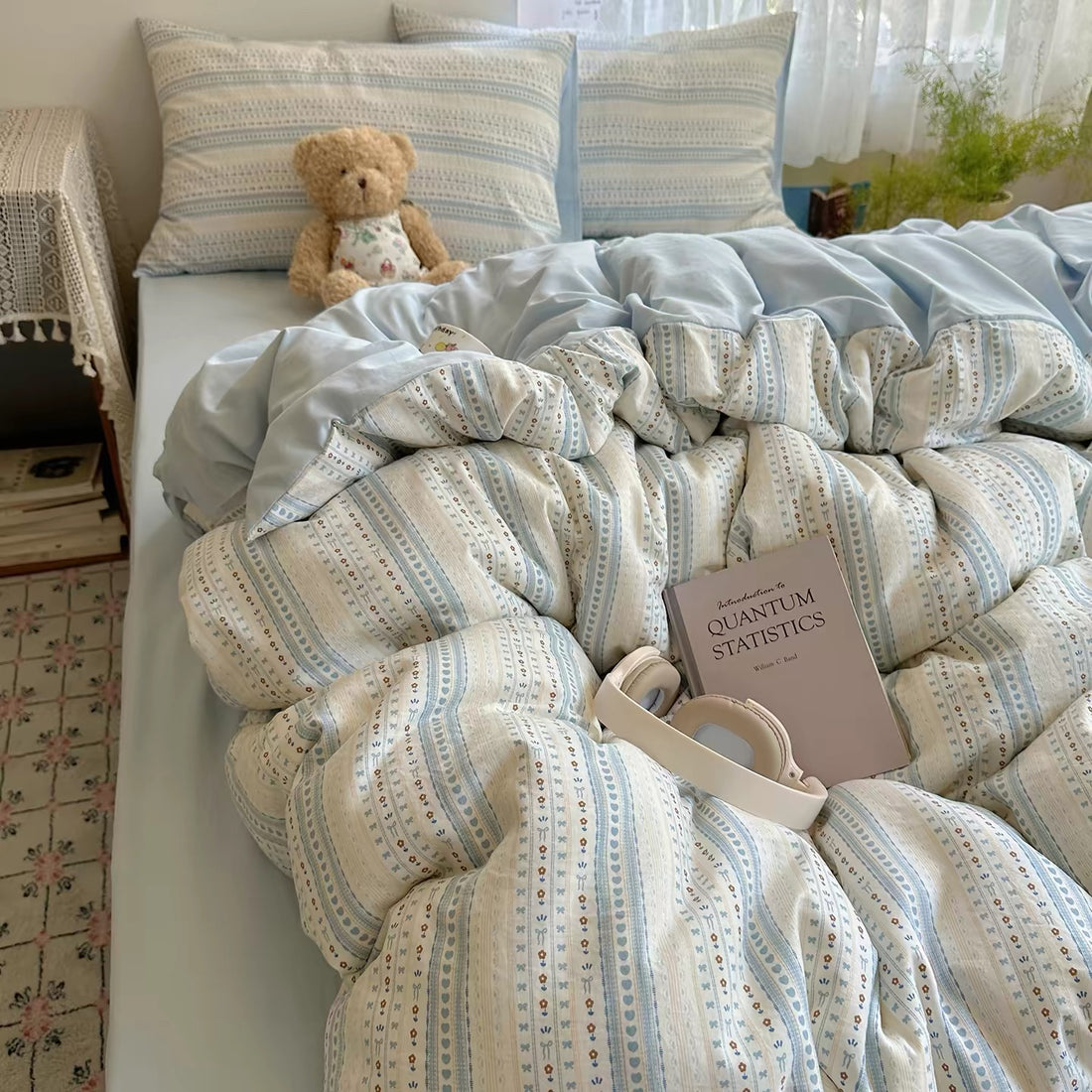 Light blue floral stripe duvet cover set styled with lace curtains, teddy bear, and soft bedding layers.