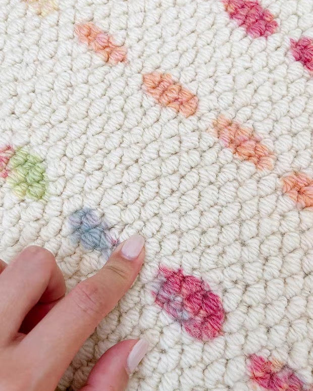 Close-up of a textured rug with colorful flower patterns and a hand for scale.