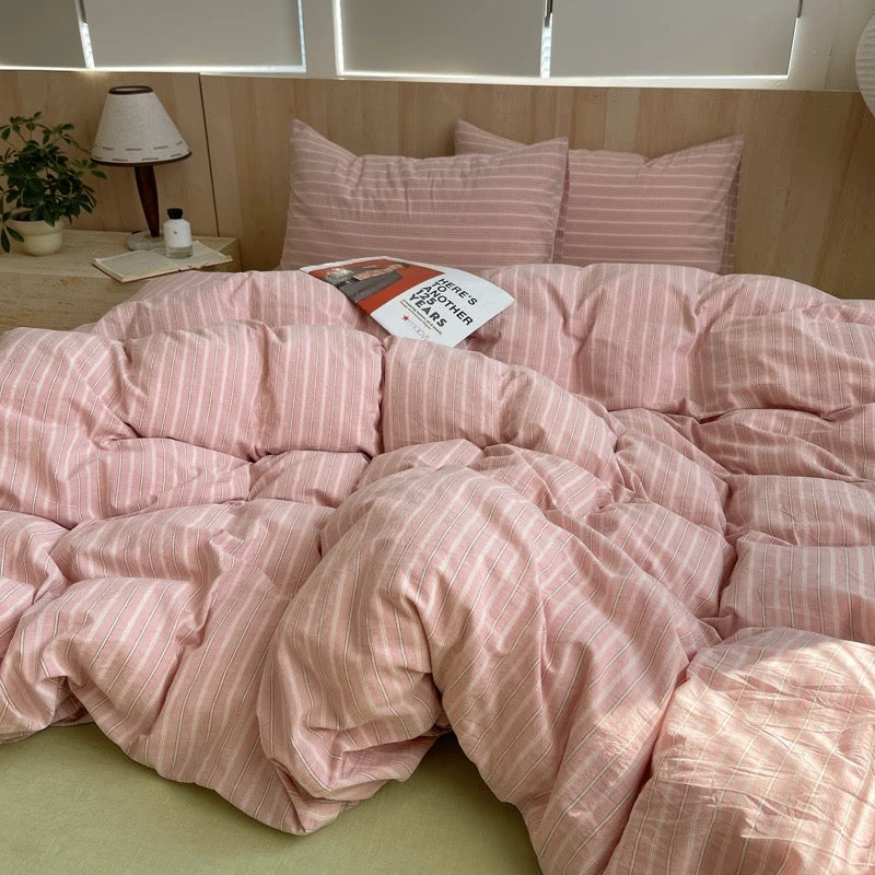 Pink striped bedding on a bed with a lamp and plant in the background
